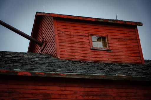 A low angle shot of a dormer on a roof of an old red building under a cloudy sky