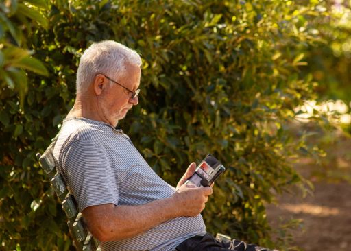 An elderly man sitting on bench and looking at smartphone in park
