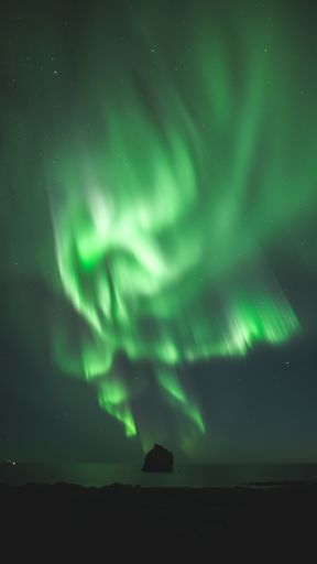A vertical shot of Northern lights illuminating the night sky in green color with long exposure