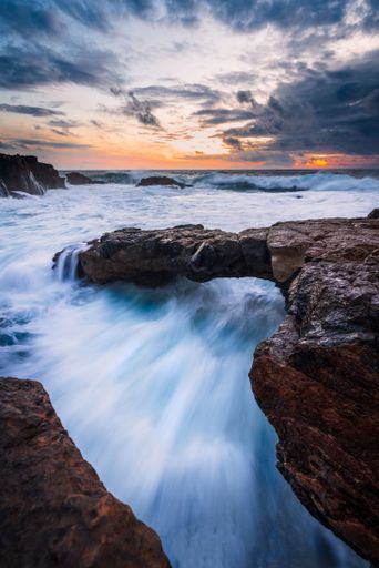 An aerial view of sea waves breaking rocky beach during sunset