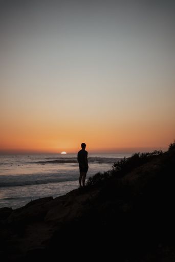 A vertical shot of a silhouette of a person standing on the seashore at sunset perfect for wallpapers