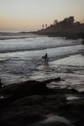 A vertical shot of a guy surfing in the sea at sunset perfect for wallpapers