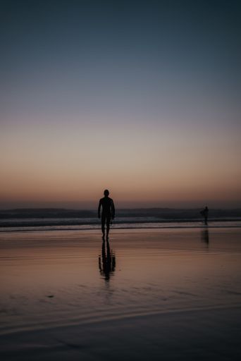 A vertical shot of a reflection of a person walking on the seashore at sunset perfect for wallpapers