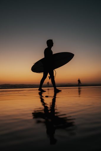 A vertical shot of a person with a surfing board walking on the beach at sunset perfect for wallpapers