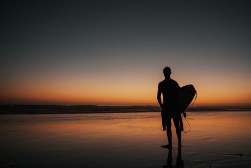 A person with a surfing board walking on the beach at sunset perfect for wallpapers and backgrounds