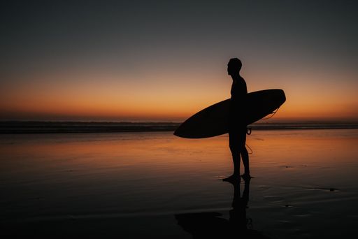 A person with a surfing board walking on the beach at sunset perfect for wallpapers and backgrounds