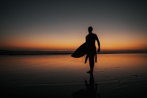 A person with a surfing board walking on the beach at sunset perfect for wallpapers and backgrounds