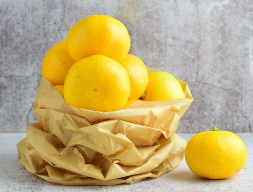 A closeup shot of a pile of yellow mandarins in a brown paper bag