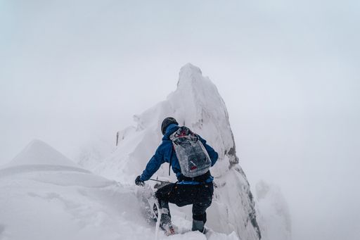 An alpinist climbing an alpine ridge in winter extreme conditions. Adventure ascent of alpine peak in snow and on rocks. Climber ascent to the summit
