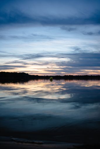 A vertical shot of the lake with the reflection of the beautiful sky surrounded by trees at sunset