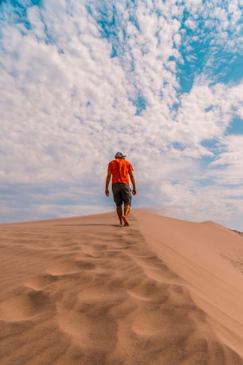 A vertical shot of a male walking in the sandy desert
