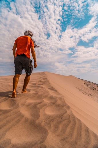 A vertical shot of a male walking in the sandy desert