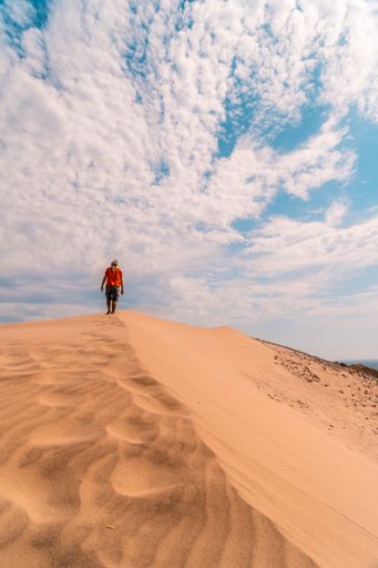 A vertical shot of a male walking in the sandy desert