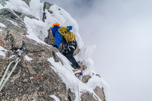 An alpinist climbing an alpine ridge in winter extreme conditions. Adventure ascent of alpine peak in snow and on rocks. Climber ascent to the summit