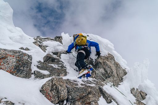 An alpinist climbing an alpine ridge in winter extreme conditions. Adventure ascent of alpine peak in snow and on rocks. Climber ascent to the summit