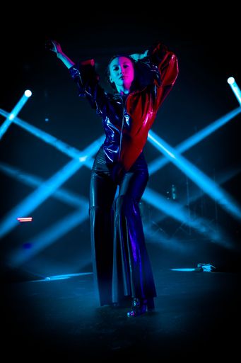 A vertical shot of an attractive woman posing on a club stage with neon lights in the background
