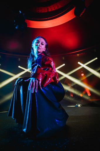 A vertical shot of an attractive woman posing on a club stage with neon lights in the background