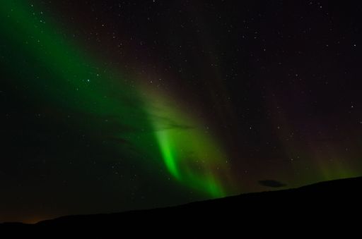 A landscape shot of the night Northern Lights coming behind the black mountains