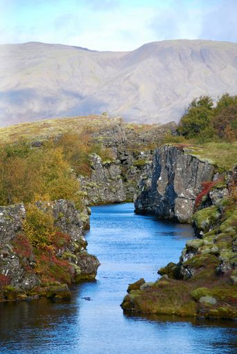 A vertical shot of calm river with the rocky shore against the mountains