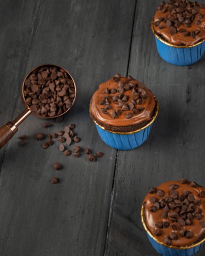 A closeup of the caramel cupcakes with chocolate chips over a wooden background