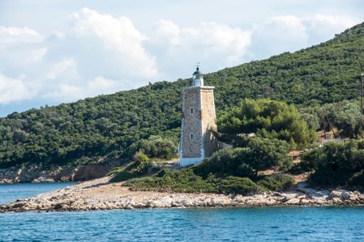 A beautiful scene of the small lighthouse by the sea surrounded by green hills in the daytime in Trikeri, Greece