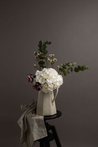 A vertical shot of a white vase with ornamental flowers placed on a wooden stand