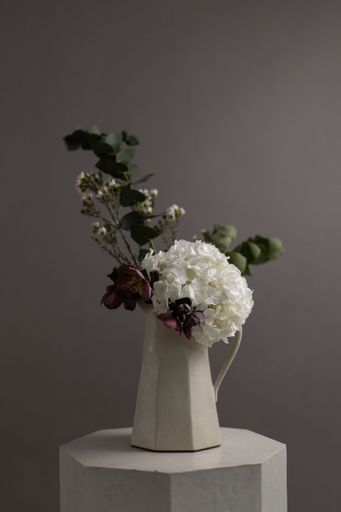 A vertical shot of a white vase with ornamental flowers placed on a stone stand in a studio