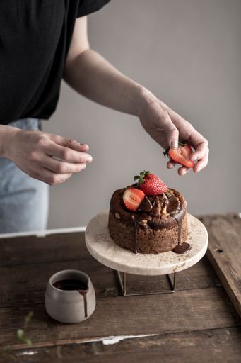 A vertical shot of a person decorating the dripping chocolate cake with strawberries
