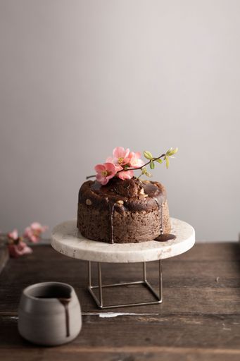 A vertical shot of a dripping chocolate cake with gentle pink flowers on a cake stand