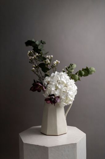 A vertical shot of a white vase with ornamental flowers placed on a stand in a studio
