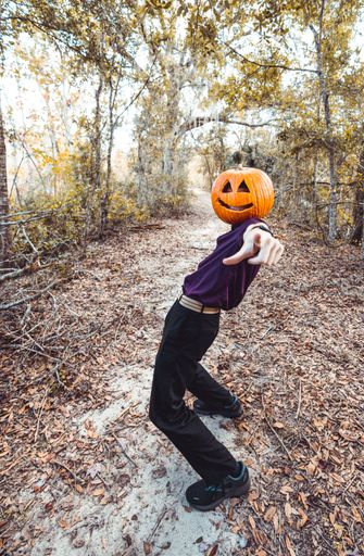A vertical shot of a cool young man wearing a carved pumpkin with a smile on his head and pointing forward