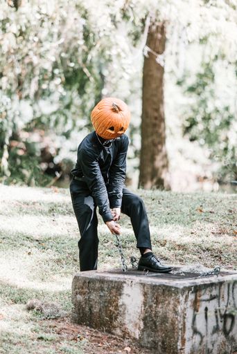 A vertical shot of a young man wearing a carved pumpkin on his head