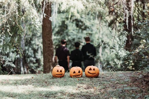 Three carved pumpkins on the grass with men dressed in black in the foreground