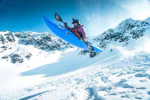 A woman making jump with ZET kayak while sliding down a snowy mountain