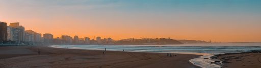 Beautiful sunset of city of Gijon in Asturias, Spain, with beach in the foreground, surfers taking waves and people walking with its dogs