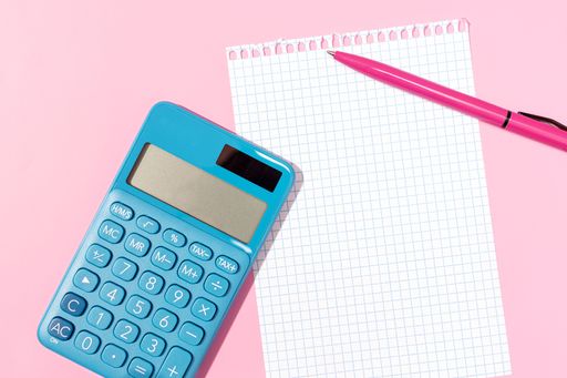 Flat lay of a calculator, blank grid paper notebook and pen on pink background. Template mock up