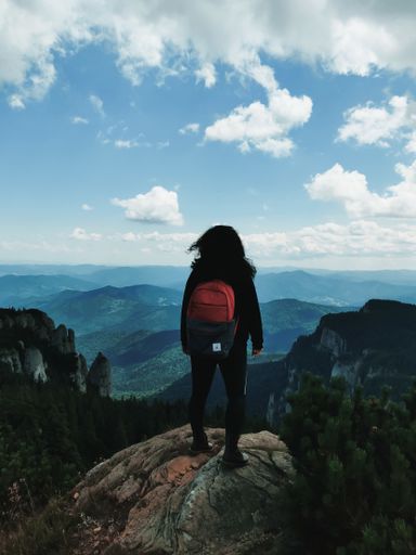 A vertical back view of a female hiker standing on a mountain looking out at the view