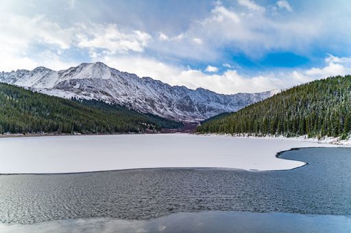 An aerial view of frozen lake surrounded by dense trees