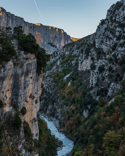 A vertical shot of a stream flowing through the hiking area Sentier Blanc-Martel with trees under the clear sky