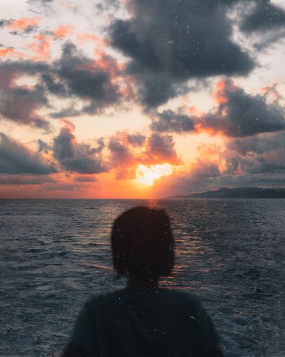 A silhouette of female looking at sea during sunset