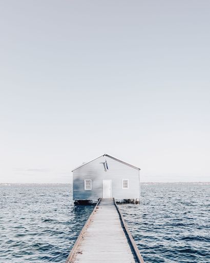 A vertical shot of a road to a house surrounded by a deep blue sea