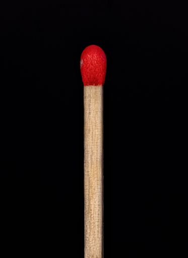 A closeup shot of a single red matchstick on a black background.