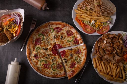 A table with a variety of foods for delivery. Beef and chicken kebab, fries, pepperoni pizza.