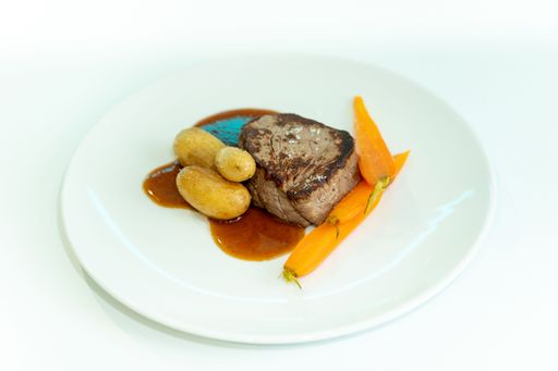 A meal of meat, potato and carrot in a white plate.