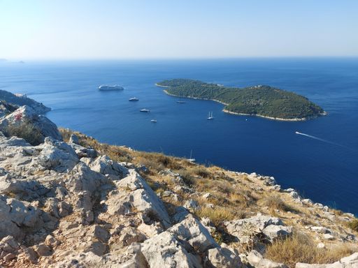 A high-angle shot of an island and ships in the ocean seen from the top of a rocky hill
