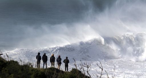 Big wave crushing in the background while people watch it from a safe distance