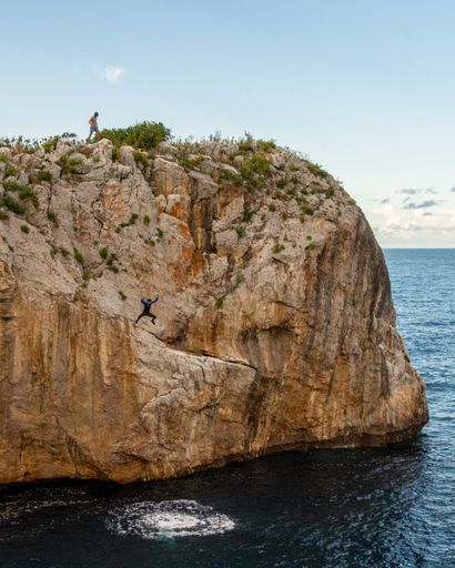 A cliff next to a sea with people jumping in it