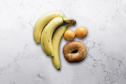 A closeup shot of a doughnut, banana, and oranges on a white surface