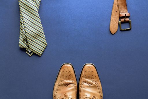 A closeup shot of shoes. tie and a belt on a dark blue surface