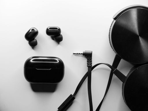 A flat lay grayscale of wireless earbuds and a headset with a wire on an isolated background